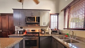 A modern kitchen with stainless steel appliances, granite countertops, and wooden cabinets. - Casa Gris with private pool near the beach in Jaco (Jacó)