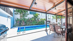 A modern outdoor pool area with a barbecue grill, dining table, and chairs. - Casa Gris with private pool near the beach in Jaco (Jacó)