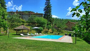 Una piscina con lettini, un gazebo e edifici in pietra sullo sfondo.