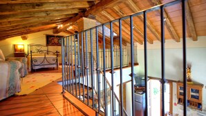 Una camera da letto rustica con soffitto in legno, ringhiera in metallo, un letto e un comodino con una lampada.
