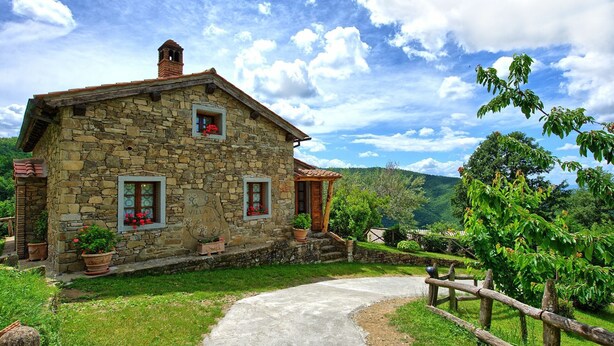 Una villa in pietra con un camino in pietra, due finestre con persiane e un piccolo portico.