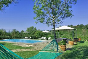 Ein Poolbereich mit Liegestühlen und einer Hängematte, umgeben von Grünpflanzen und einer Pergola.