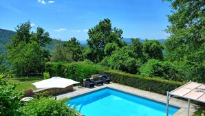 A rectangular swimming pool with a stone border, surrounded by lush greenery and trees. - Villa Margherita Uno - Holiday Villa Rental with swimming pool in Cortona, Tuscany (Cortona)