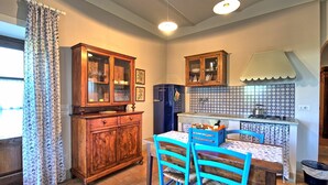 A kitchen with wooden cabinets, a blue refrigerator, a tiled backsplash, and a dining area with blue chairs and a table. - Stalla - Country House Rental in Valdichiana, Tuscany (Gabbiano)
