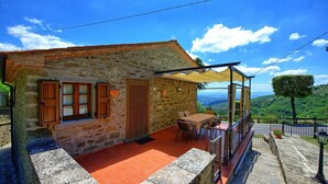 A stone house with a patio, wooden shutters, and a table with chairs. - Villa Portole Uno - Holiday Villa Rental in Cortona (Tornia)