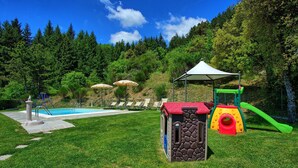 A backyard with a swimming pool, a children's play area, and a covered seating area.