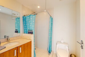 Une salle de bain équipée d’un lavabo, d’un miroir, de toilettes et d’un rideau de douche.