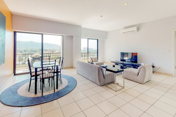 Un salon moderne comprenant un coin repas, un canapé, un téléviseur et un balcon offrant une vue sur la ville.