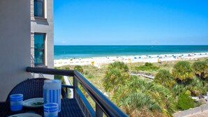 Ein Balkon mit Blick auf einen Strand, Palmen und einen klaren, blauen Himmel.