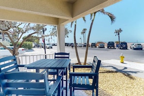 An outdoor seating area with tables and chairs, a fire hydrant, and a view of the beach and parked cars.