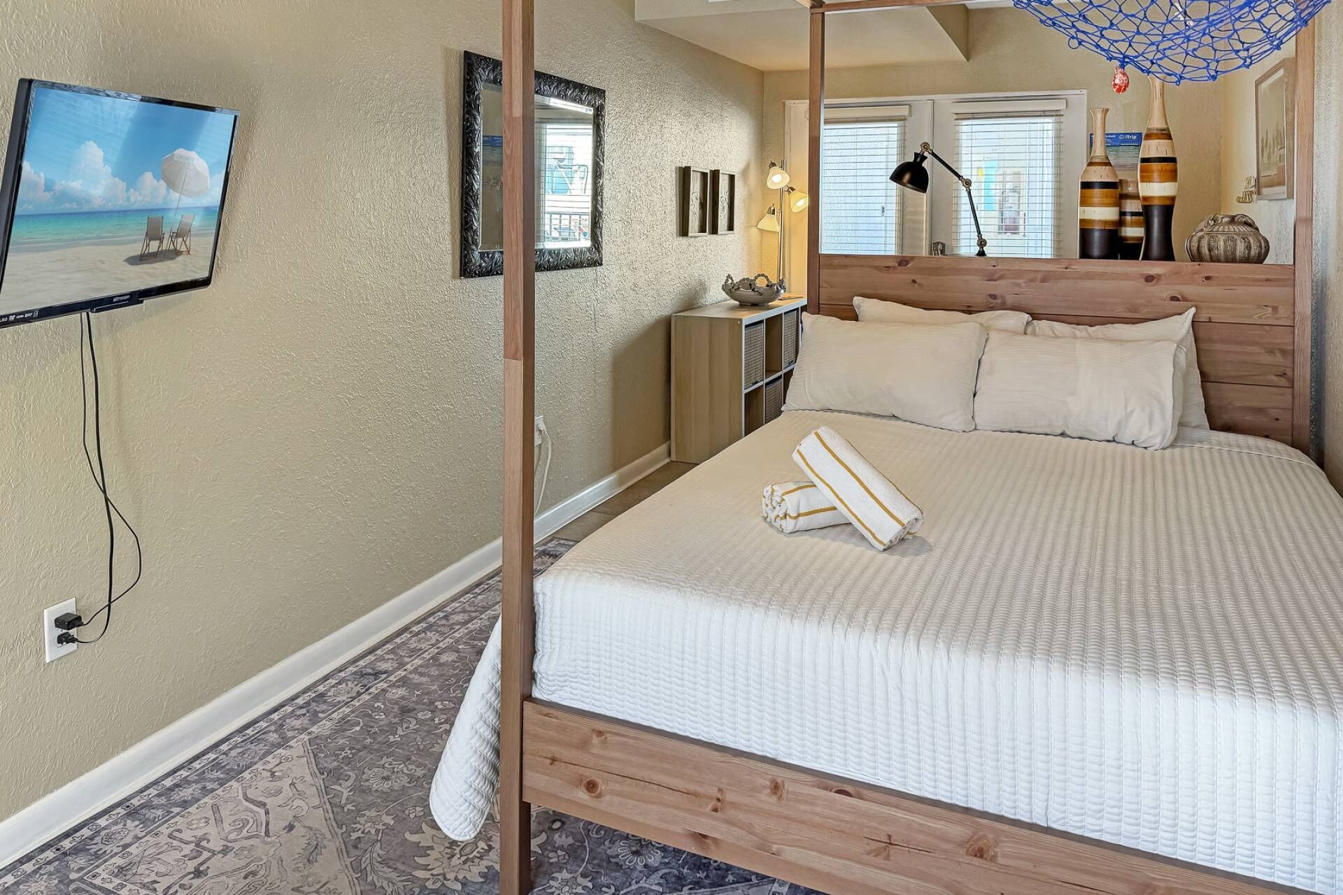 A bedroom with a bed, a TV, a nightstand, and a window with blinds.