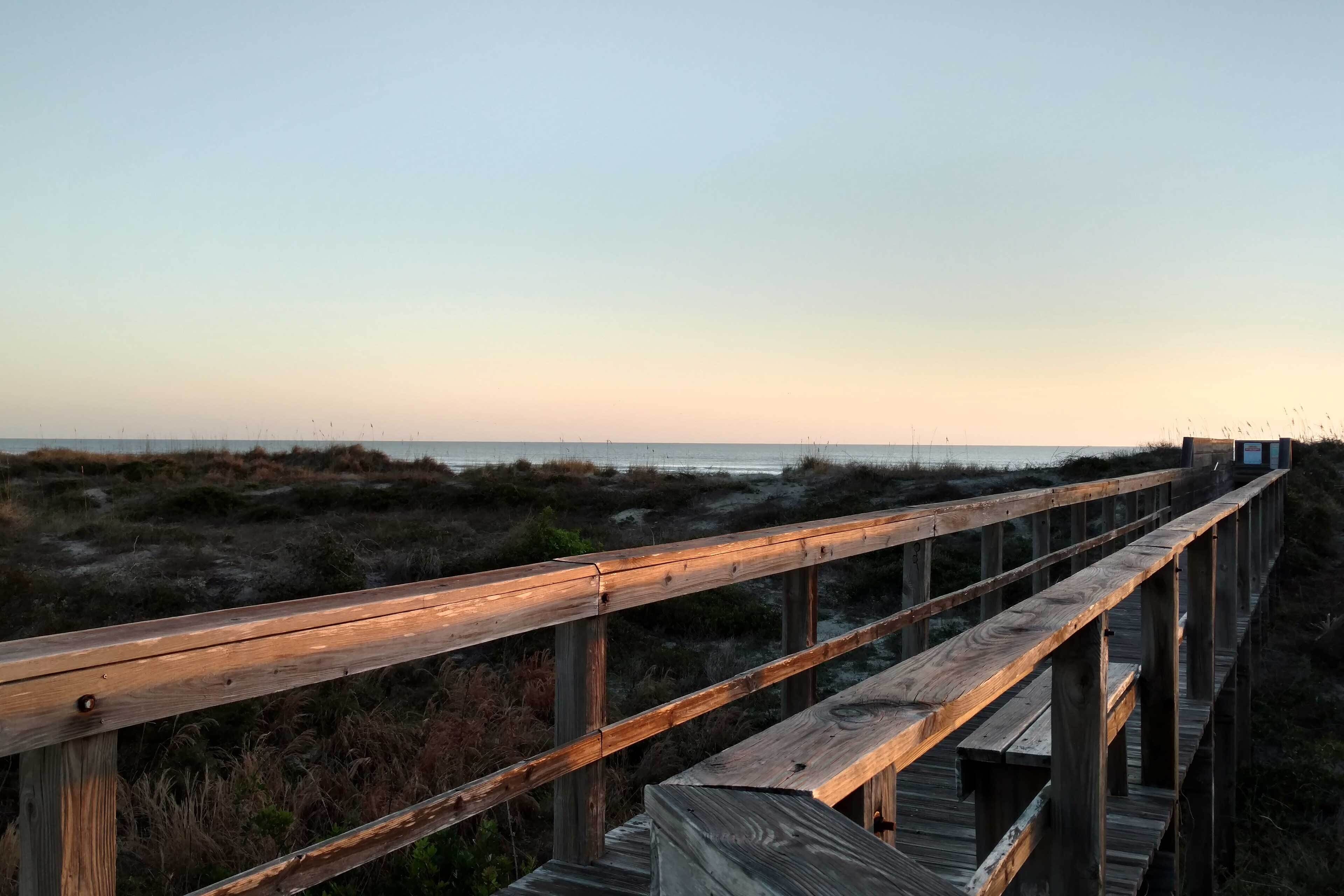 A wooden boardwalk leading to a beach with a clear sky.