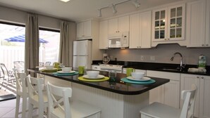 Een moderne keuken met witte kasten, een zwart aanrecht en een centraal eiland met barstoelen.