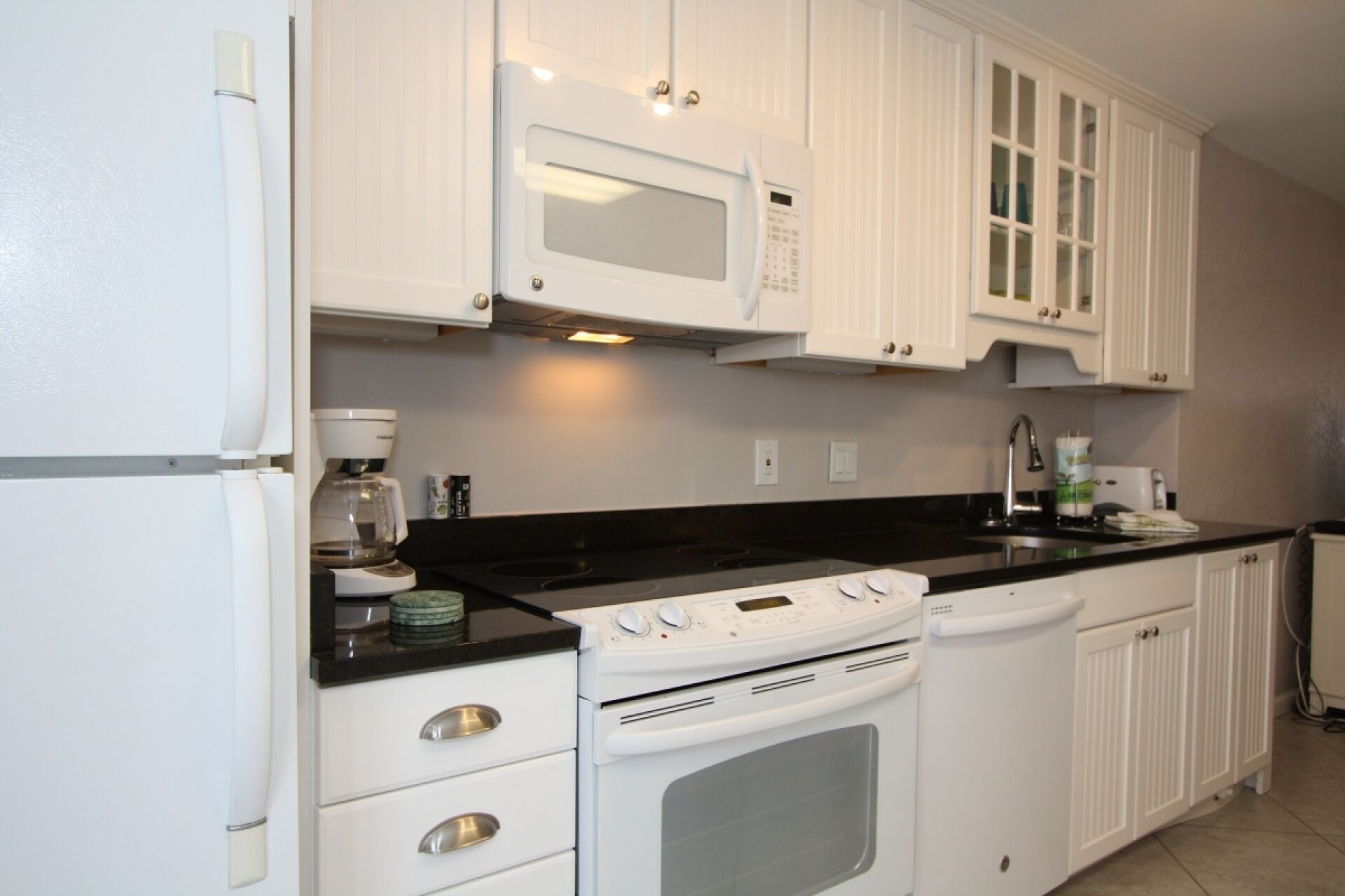 A kitchen with white cabinets, a black countertop, a microwave, an oven, and a coffee maker.
