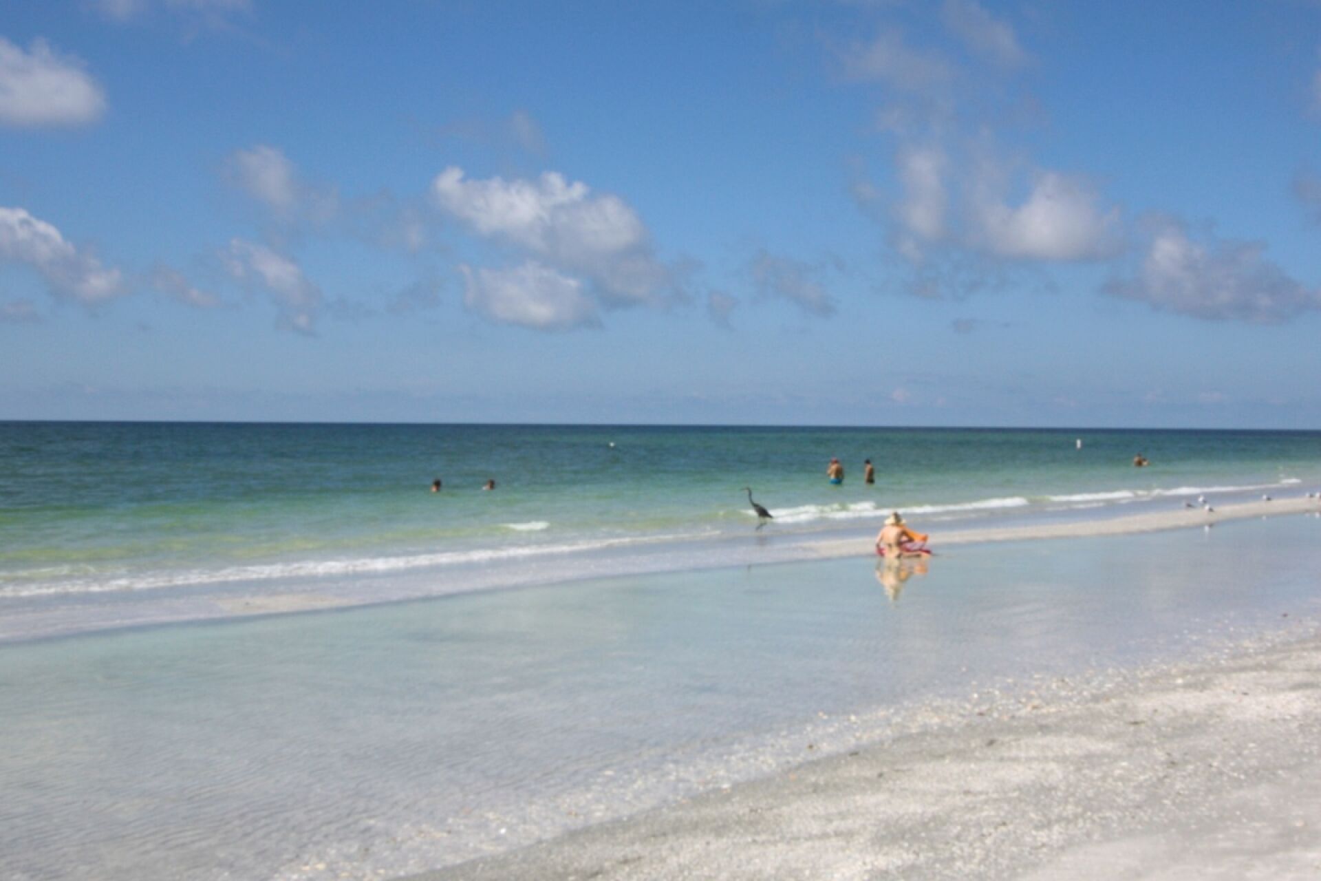 Una playa con aguas cristalinas, orilla arenosa y algunas personas a lo lejos.