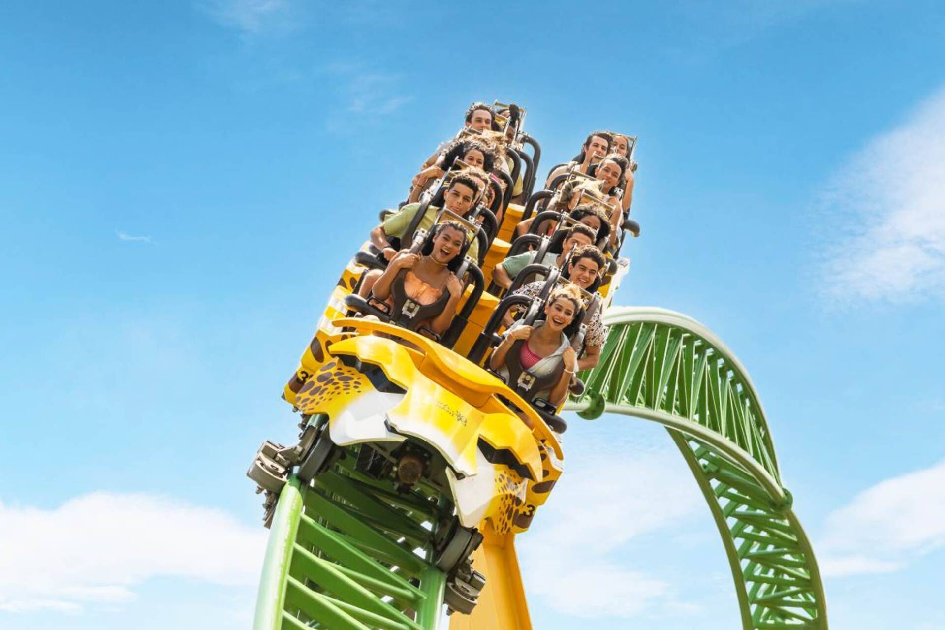 A roller coaster with passengers in a yellow and green car, set against a clear blue sky.
