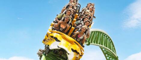 A roller coaster with passengers in a yellow and green car, set against a clear blue sky.