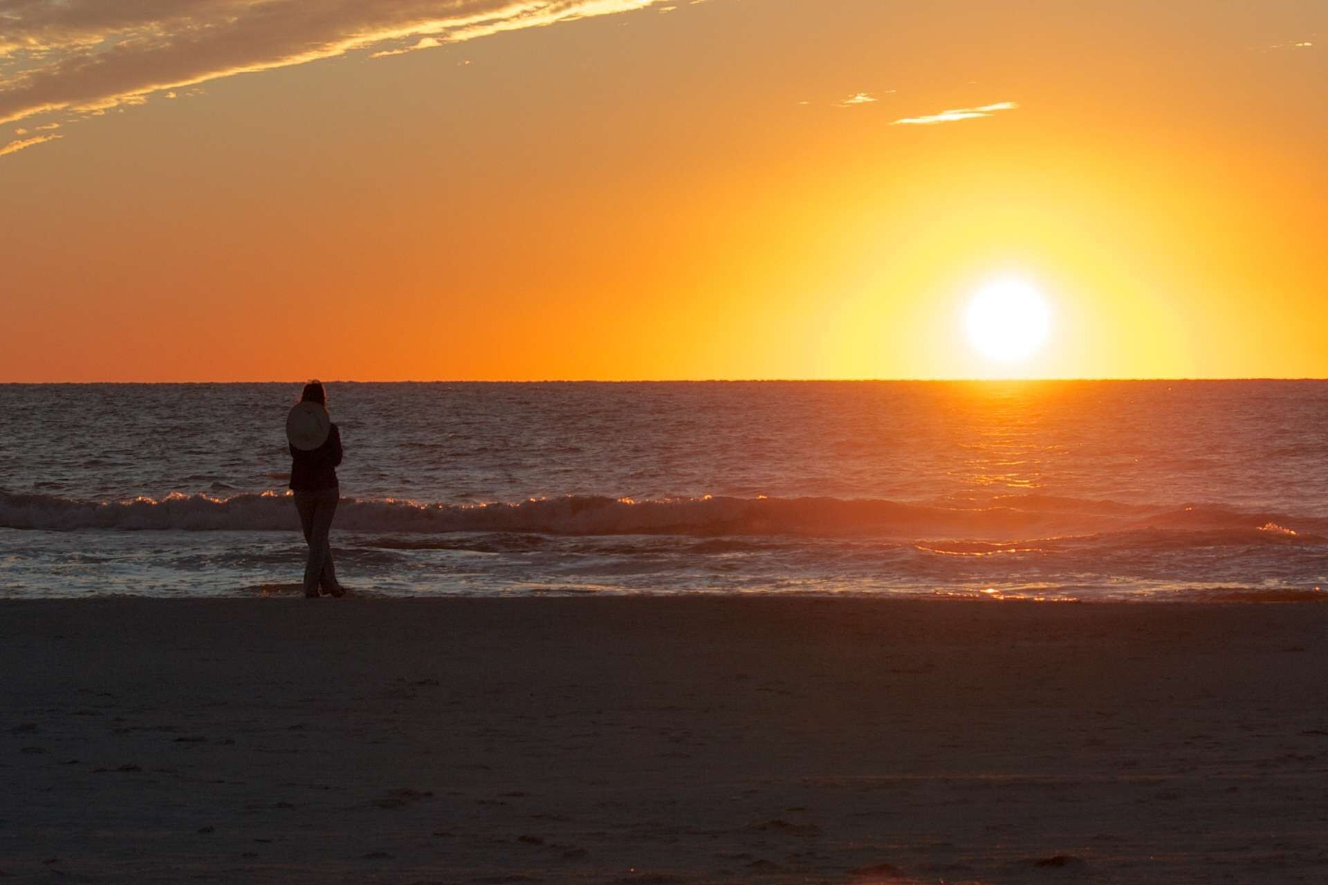 A person standing on a beach during sunset.