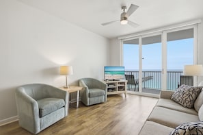 A living room with a sofa, two armchairs, a TV, and a balcony with a view.