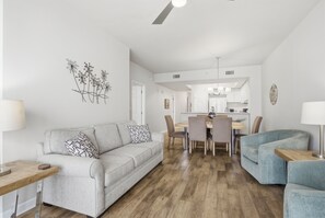 Un salon moderne avec un canapé gris, un fauteuil bleu et un coin repas doté d’un plancher en bois et de murs blancs.