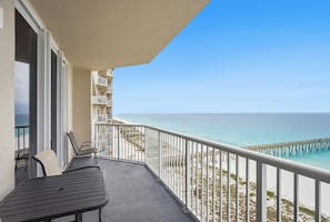 A balcony with a table and chairs, overlooking a beach and a pier.