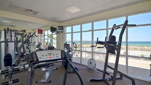 Ein Fitnessstudio mit Cardiogeräten und Gewichten, große Fenster mit Blick auf den Strand.