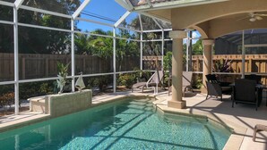 A pool area with clear water, surrounded by a glass enclosure, and furnished with chairs and tables. - Superb Naples Home w/ Den & Private Saltwater Pool (Naples)