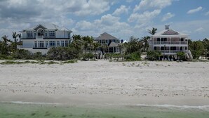 A beachfront property with multiple houses, a sandy beach, and palm trees. - Manatee Manor: Exclusive Beachfront Retreat with Gulf Views (North Captiva)