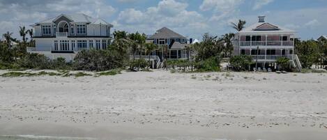 A beachfront property with multiple houses, a sandy beach, and palm trees.