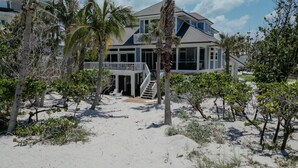 A beachfront property with a two-story house, a covered deck, and a staircase leading to the entrance. - Manatee Manor: Exclusive Beachfront Retreat with Gulf Views (North Captiva)