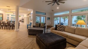 A spacious living area with a high ceiling fan, large windows, and a view of palm trees. - Manatee Manor: Exclusive Beachfront Retreat with Gulf Views (North Captiva)