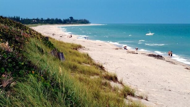 A beach with clear blue water, a boat in the distance, and people walking along the shore. - Tropical Cottage < 2 Mi to Hobe Sound Beach! (Hobe Sound)
