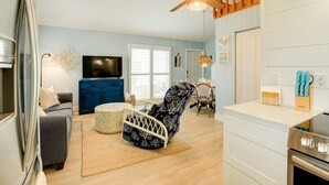 A modern living room with a sofa, a patterned chair, a television, and a kitchen area with a stove. - Tropical Cottage < 2 Mi to Hobe Sound Beach! (Hobe Sound)