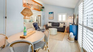 A modern living room with a dining area, featuring wicker furniture, a blue accent wall, and a staircase. - Tropical Cottage < 2 Mi to Hobe Sound Beach! (Hobe Sound)
