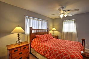 Une chambre à coucher avec un lit, deux tables de chevet avec des lampes, un ventilateur de plafond et des rideaux aux fenêtres.