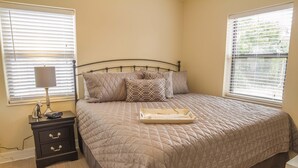 A bedroom with a bed, bedside table, lamp, and two windows with blinds. - Beach Villa ~ Pet Friendly ~ Fenced Yard ~ Steps to the Beach!!! (Saint Augustine)