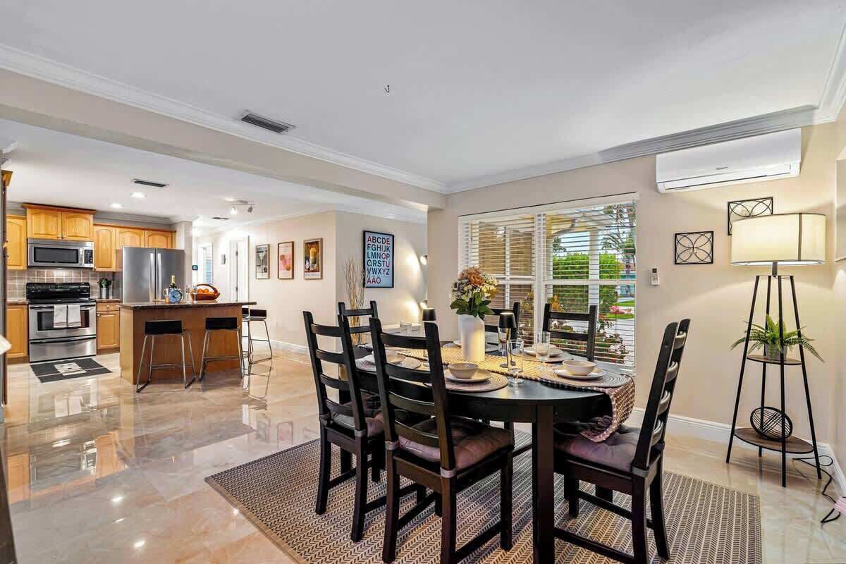 A modern kitchen with stainless steel appliances, a dining area with a round table and chairs, and a view of the outdoors through large windows.