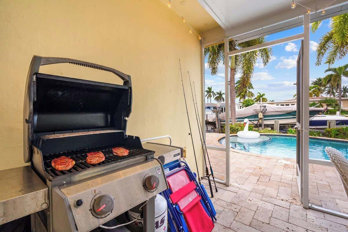 A grill with burgers cooking, a pool with a swan float, and a view of palm trees.