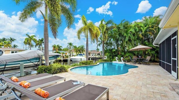 A pool area with lounge chairs and a swan statue, surrounded by palm trees and a clear sky. - Waterfront 3BR Home w/ Heated Pool & Kayaks (Pompano Beach)