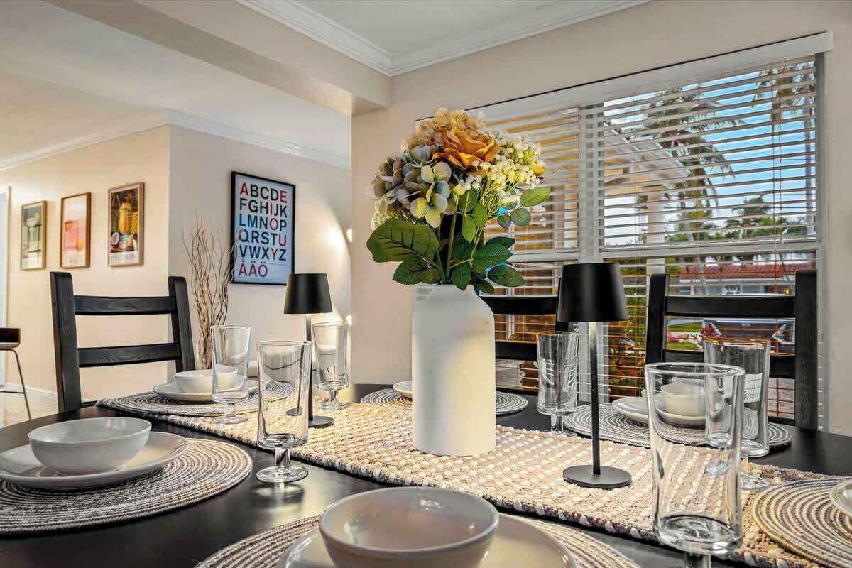A dining table set with placemats, plates, glasses, and a vase with flowers.