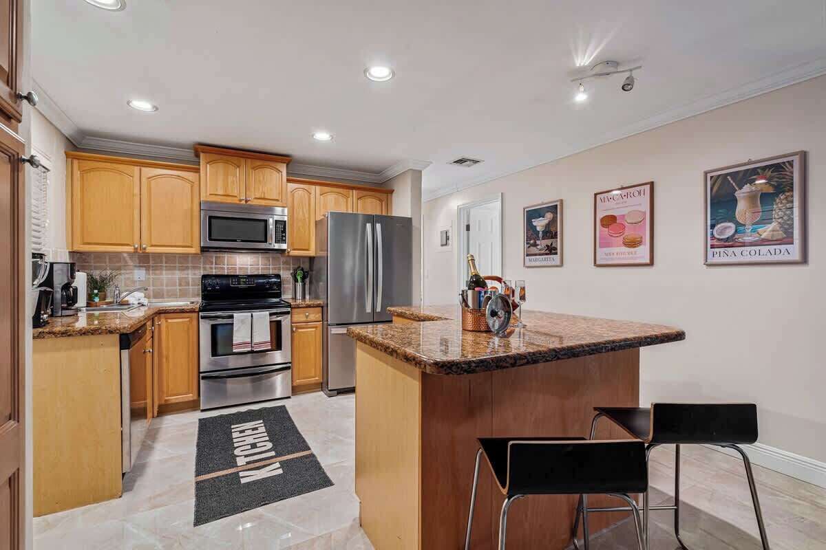 A modern kitchen with wooden cabinets, stainless steel appliances, a granite countertop, and a bar area with two stools.