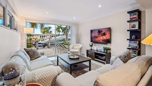 A modern living room with a sofa, coffee table, and a TV. There is a bookshelf with books and a painting on the wall. - Waterfront 3BR Home w/ Heated Pool & Kayaks (Pompano Beach)
