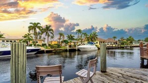 A marina with boats docked, a wooden dock with chairs, and palm trees in the background. - Waterfront 3BR Home w/ Heated Pool & Kayaks (Pompano Beach)