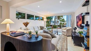 A modern living room with a sofa, coffee table, and a TV on a wall. - Waterfront 3BR Home w/ Heated Pool & Kayaks (Pompano Beach)