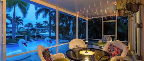 A cozy outdoor seating area with wicker chairs and a glass table, overlooking a swimming pool with swan-shaped floats.