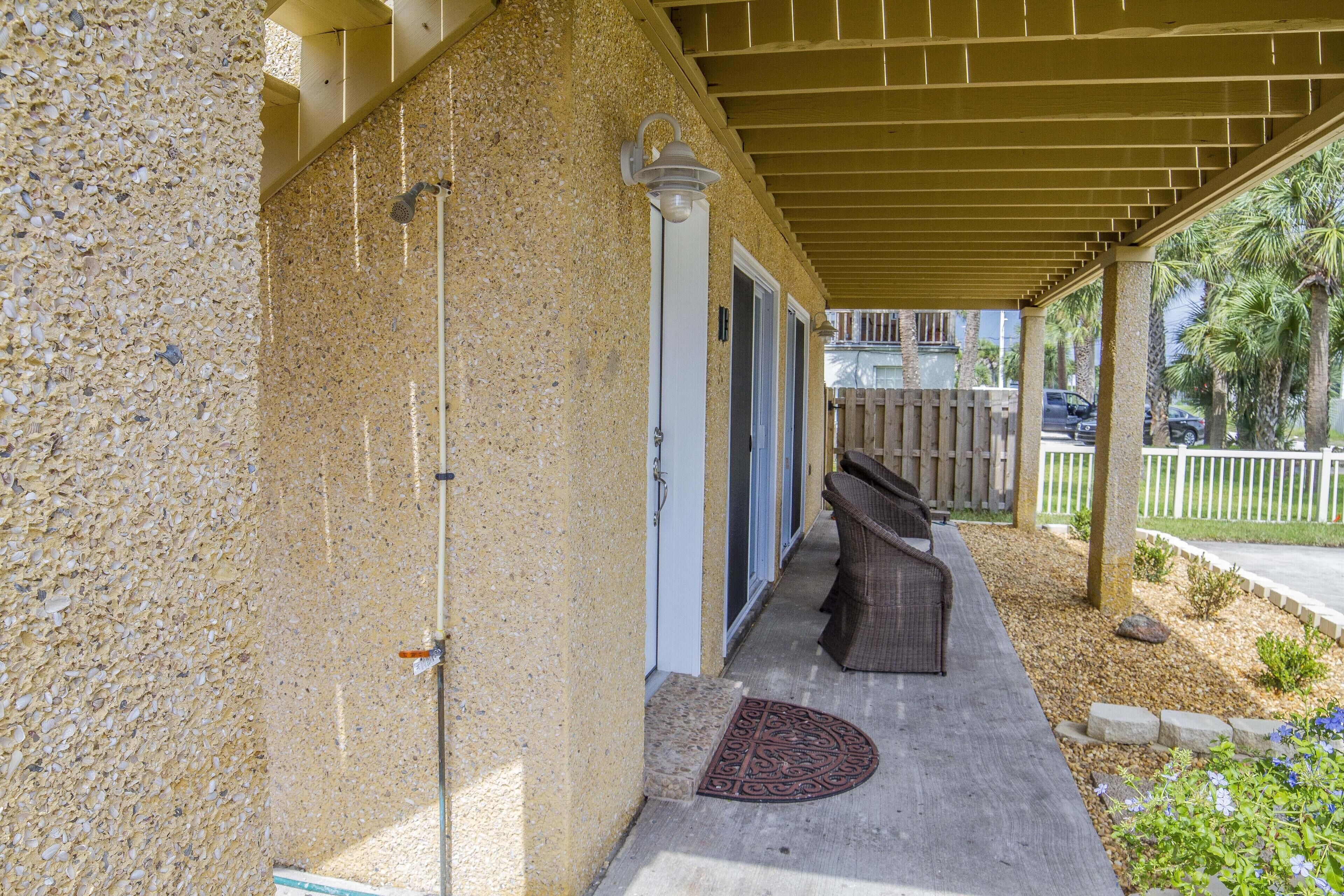 A covered outdoor area with a concrete floor, a wooden bench, and a door leading to a building.