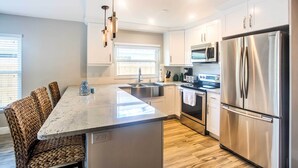 A modern kitchen with a central island, stainless steel appliances, and a dining area with woven chairs. - Naples Home w/ Lanai & Pool Near Vanderbilt Beach! (Naples)