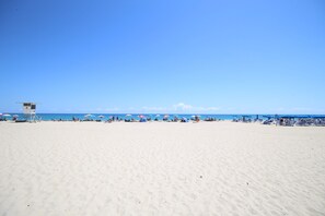 A wide sandy beach with a lifeguard tower and umbrellas. - Singer Island Condo: Walk to Beach & Marina! (Riviera Beach)
