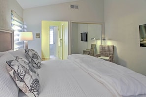 Habitación de hotel con cama, una silla, televisor y puerta que da a otra habitación.
