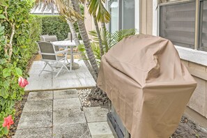 Una parrilla cubierta, una mesa de jardín con sillas y un jardín con diversas plantas y una flor rosa.